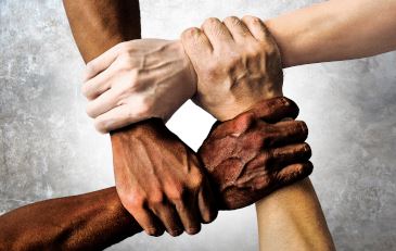 Four hands of varying skin tones holding one another